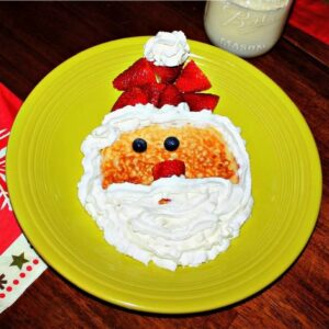 A plate with pancakes that look like Santa with fruit and whipped cream