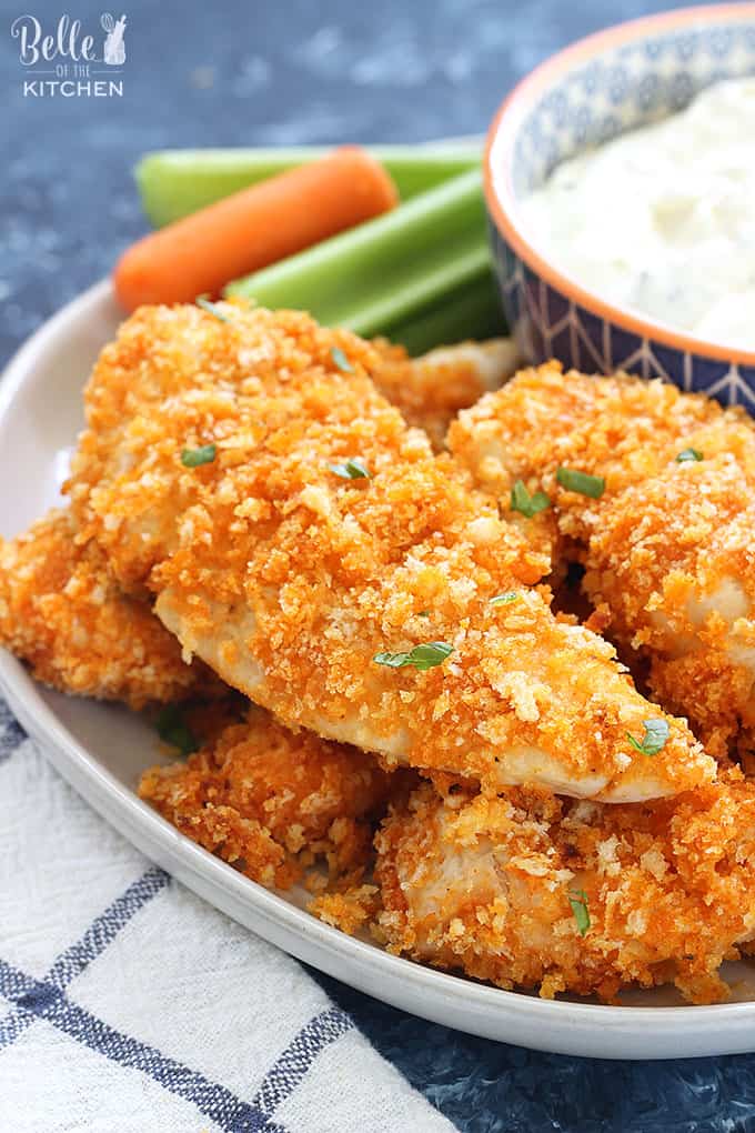 A close up of a plate of chicken tenders with carrots and celery in the background