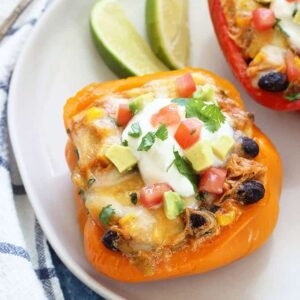 A plate of sliced peppers filled with chicken enchilada filling and sliced limes on the side