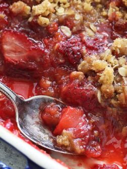 A close up of a bowl of food, with strawberry crisp and a spoon