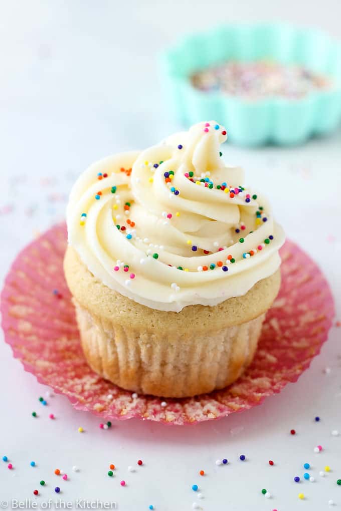 A close up of a vanilla cupcake with sprinkles on top