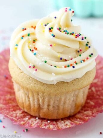 A close up of a vanilla cupcake with sprinkles on top