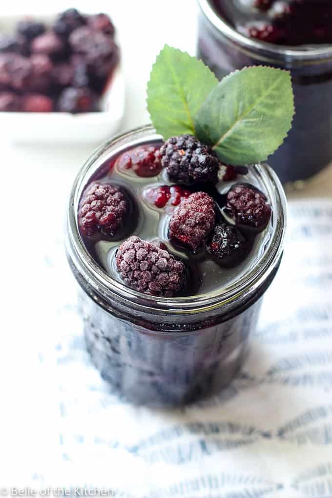 mason jar filled with blackberry sweet tea and frozen blackberries, and a small white bowl of blackberries