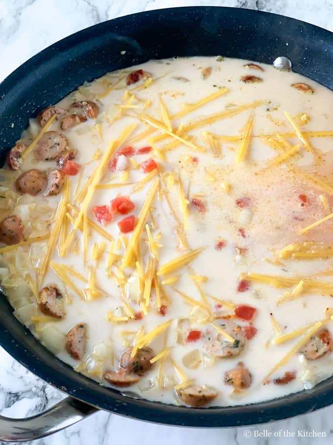 A skillet with uncooked noodles, sauce, and sausage