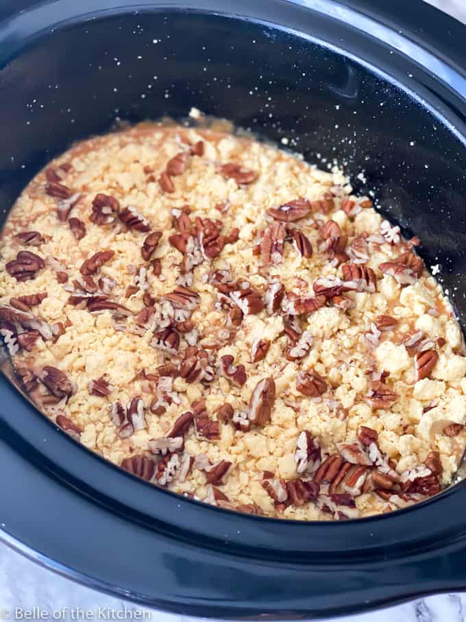 A crockpot with unbaked cake with pecans on top