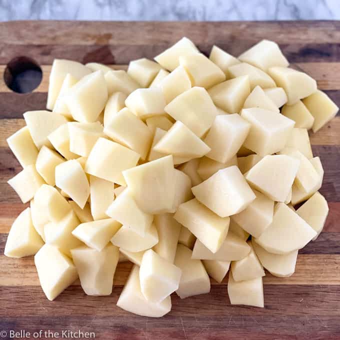 A wooden cutting board topped with chopped potatoes