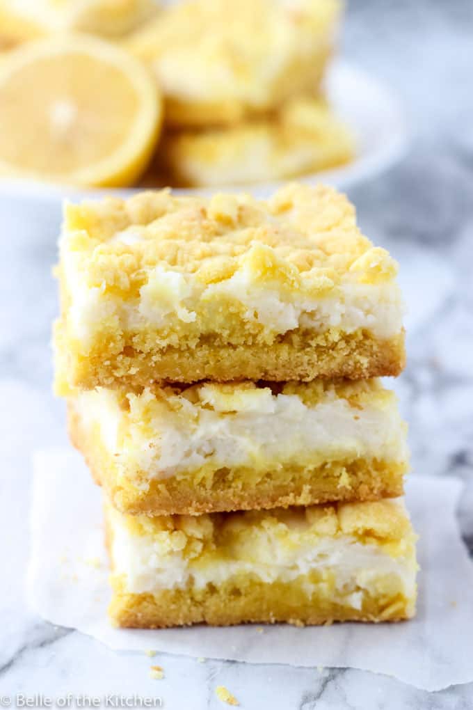 stack of three lemon cheesecake bars with plate of lemon and more bars in the background