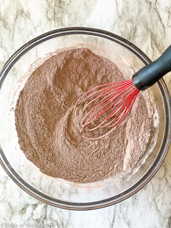 overhead shot of dry ingredients for chocolate cake with a red whisk