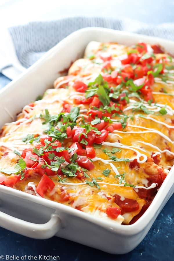 white rectangle casserole dish with enchiladas, diced tomatoes, cilantro, and sour cream