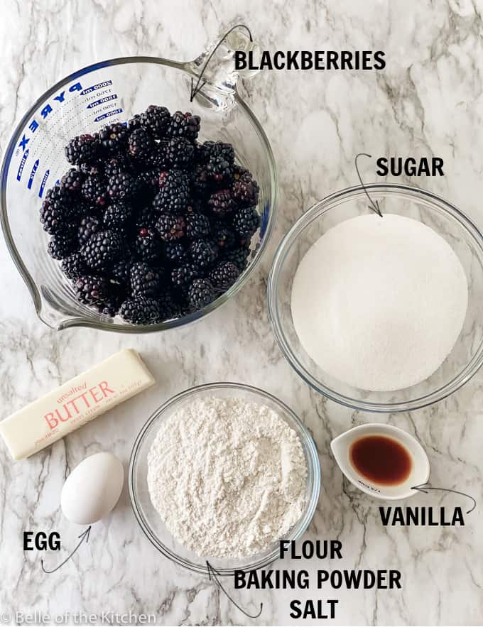 ingredients laid out on a marble backdrop; blackberries, sugar, flour, butter, egg, and vanilla