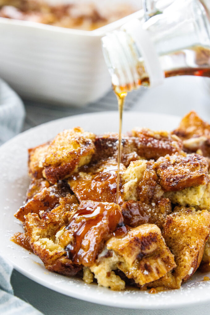 a white plate with french toast casserole and syrup poured over the top