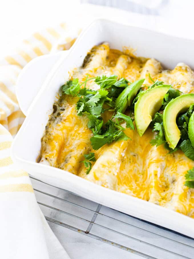 white being dish with chicken enchiladas and avocado on top