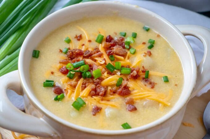 A bowl of potato soup with a spoon topped with bacon, cheese, and green onions