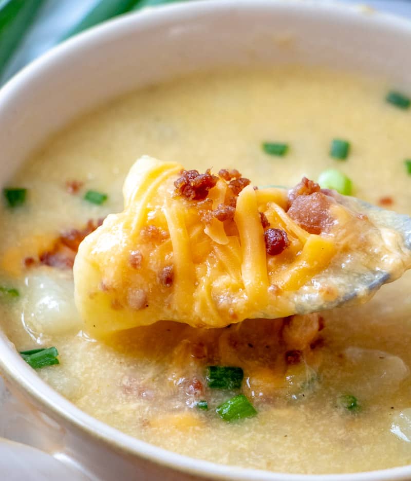 A bowl of potato soup with a spoon topped with bacon, cheese, and green onions