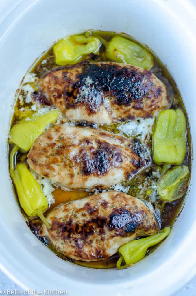 cooked chicken in a crockpot bowl surrounded by peperoncini peppers