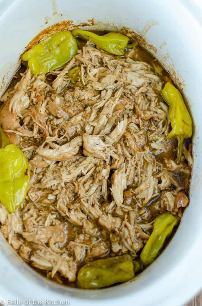 shredded chicken in a crockpot bowl surrounded by peperoncini peppers.