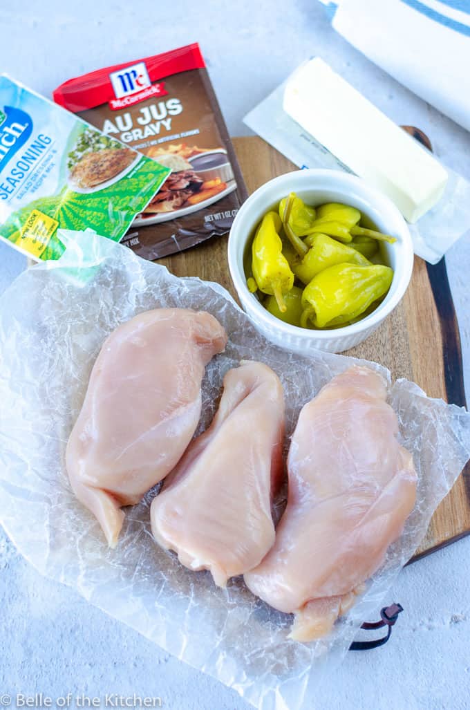 chicken breasts, seasoning packets, and a bowl of peperoncini peppers on a wooden cutting board