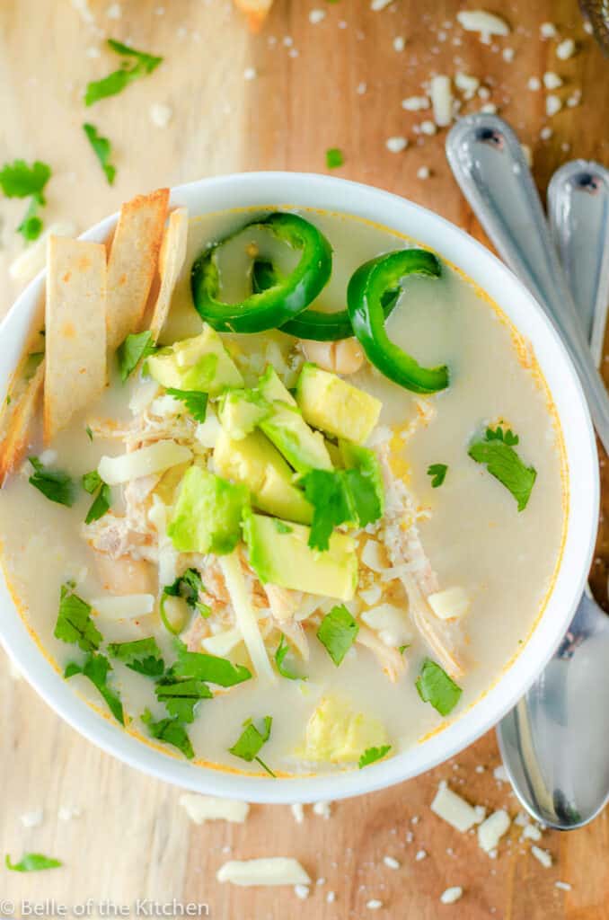 white soup bowl of chicken chili topped with jalapeños and avocado
