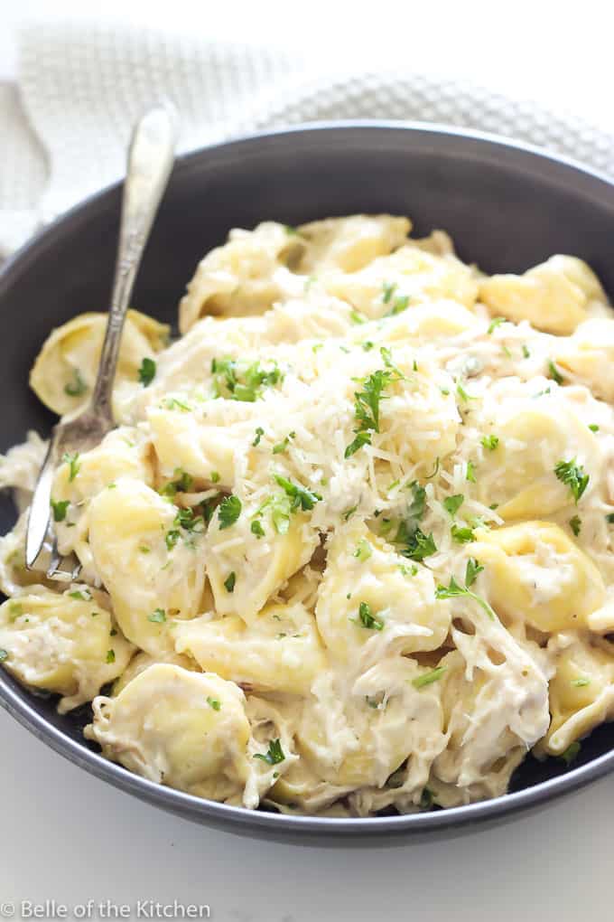 a black plate with tortellini and Chicken Alfredo