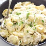 a black plate with tortellini and Chicken Alfredo