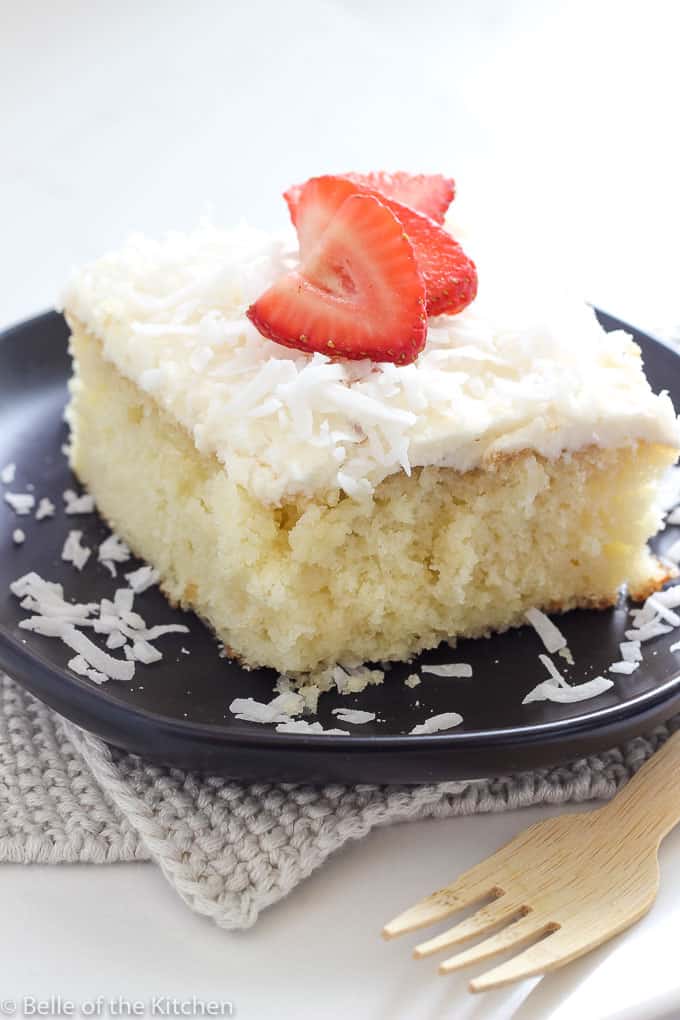 a slice of coconut cake on a black plate with strawberries on top