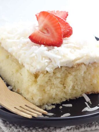 a slice of coconut cake on a black plate with strawberries on top