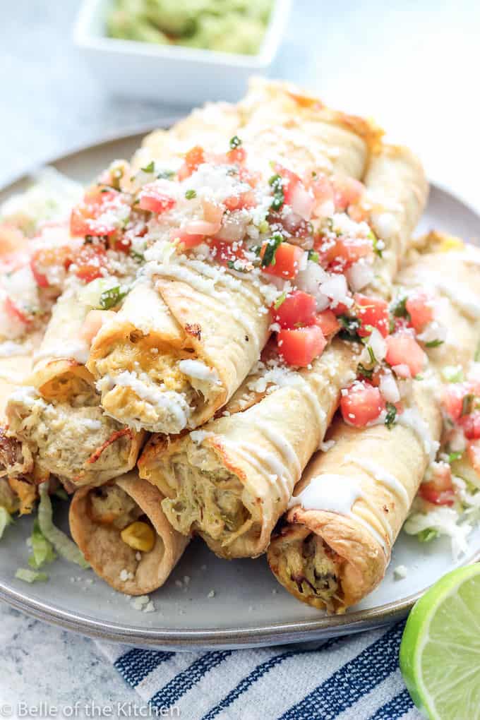 taquitos on a plate topped with pico, cheese, and lettuce