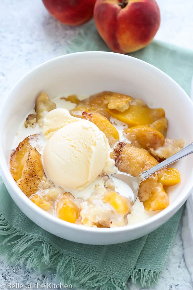 peach cobbler in a white bowl with vanilla ice cream