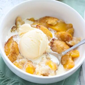 peach cobbler in a white bowl with vanilla ice cream