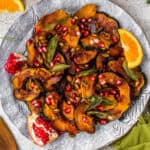 acorn squash slices topped with sage and pomegranate seeds on a plate with orange slices