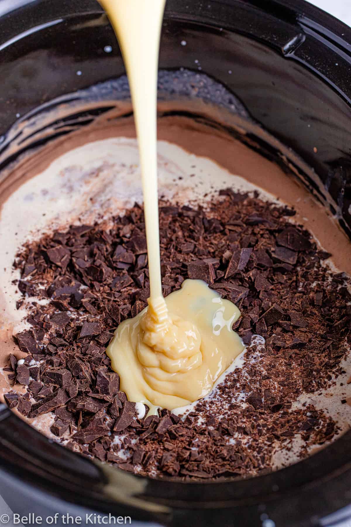 condensed milk is being poured into a crockpot of milk and chocolate