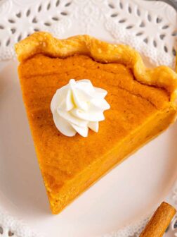 a slice of sweet potato pie on a white plate with whipped cream on top