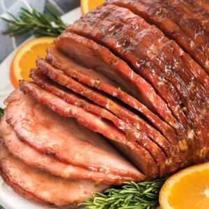 a sliced ham next to oranges and rosemary