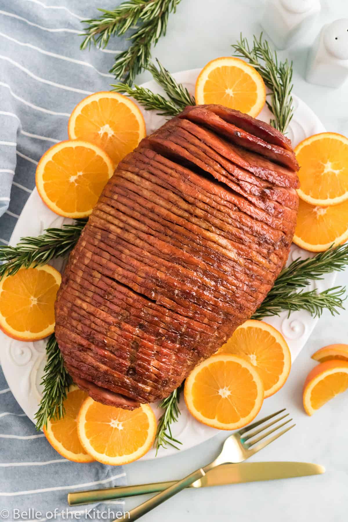 a sliced ham next to oranges and rosemary