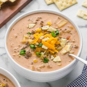 a bowl of cheeseburger soup with a spoon and crackers