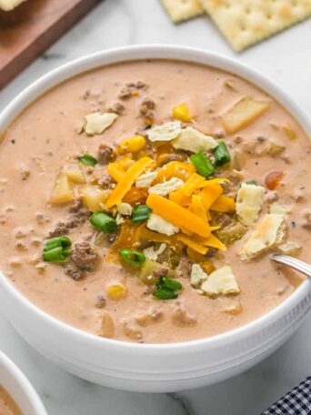 a bowl of cheeseburger soup with a spoon and crackers