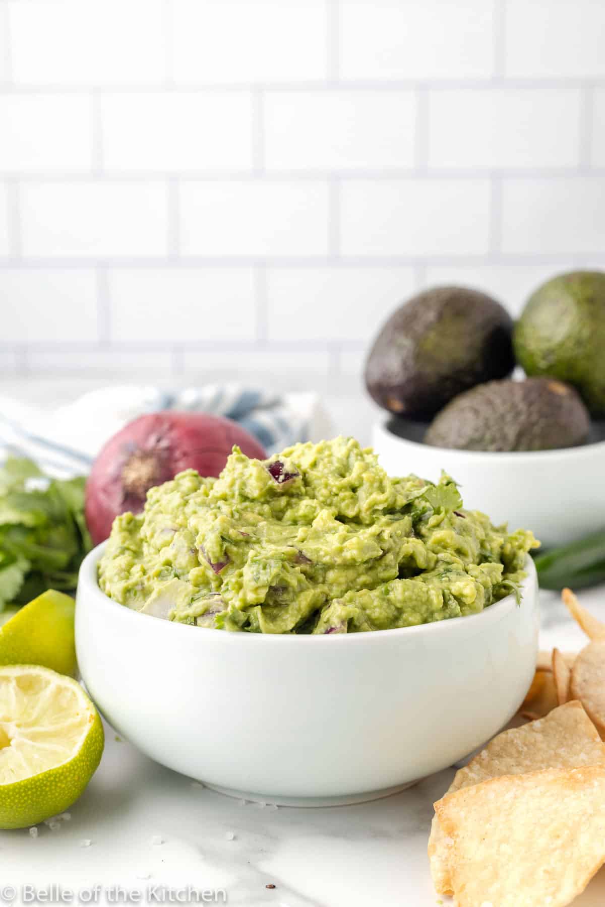 avocados in a bowl next to onions and copycat chipotle guacamole