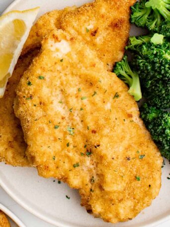 breaded chicken cutlets on a plate with lemon and broccoli