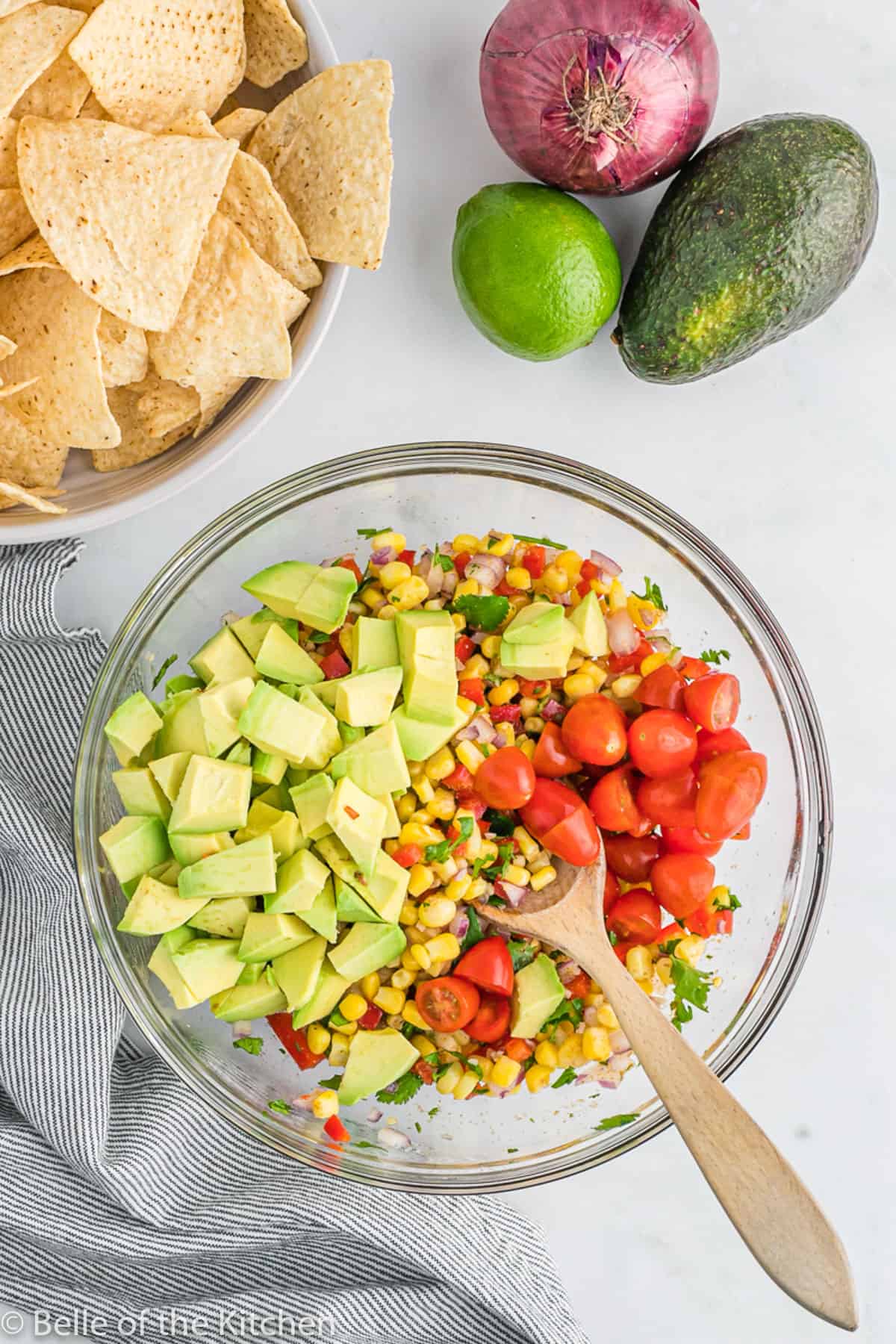 a wooden spoon mixing corn, avocado, and tomatoes