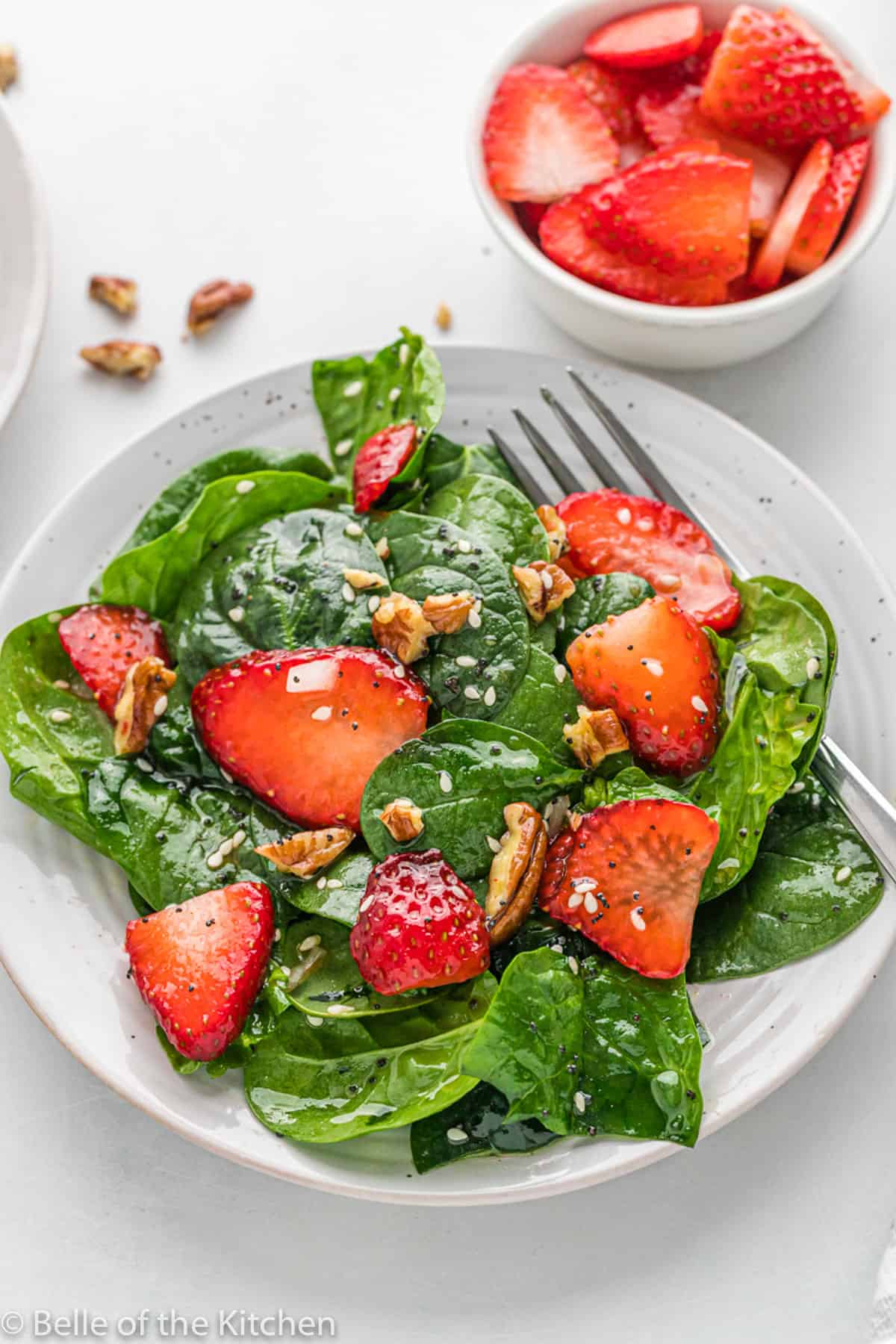 a white plate with a spinach salad topped with strawberries