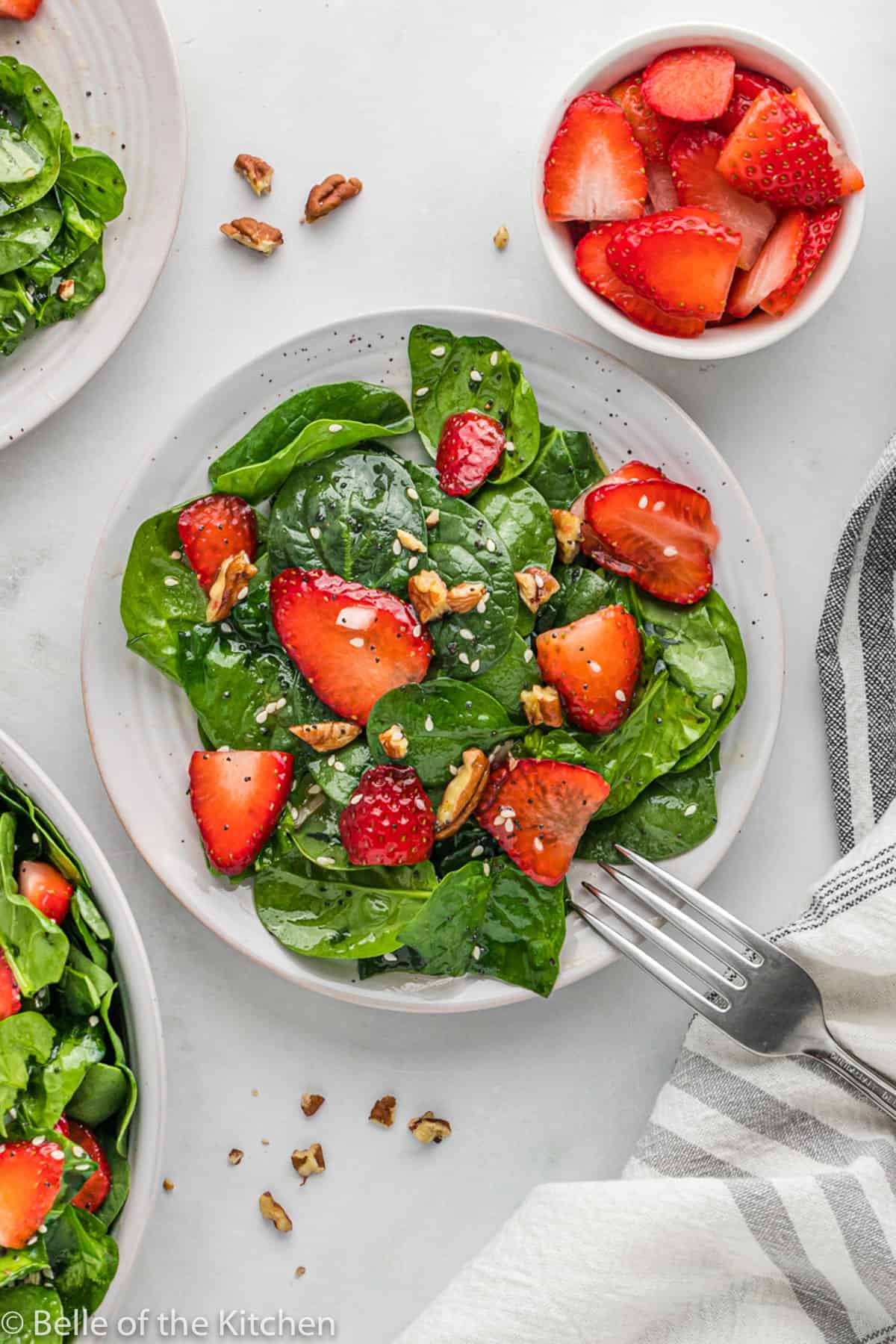 a white plate with a spinach salad topped with strawberries and a fork