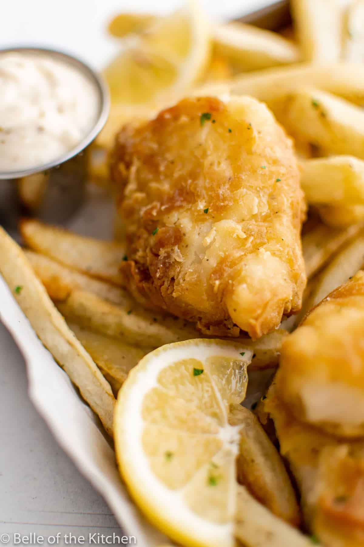 a piece of air fried fish on a tray with fries and lemon slices