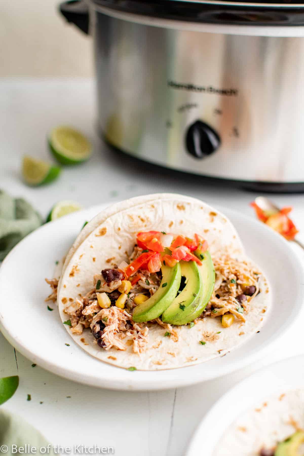 chicken tacos on white plates next to a crockpot.