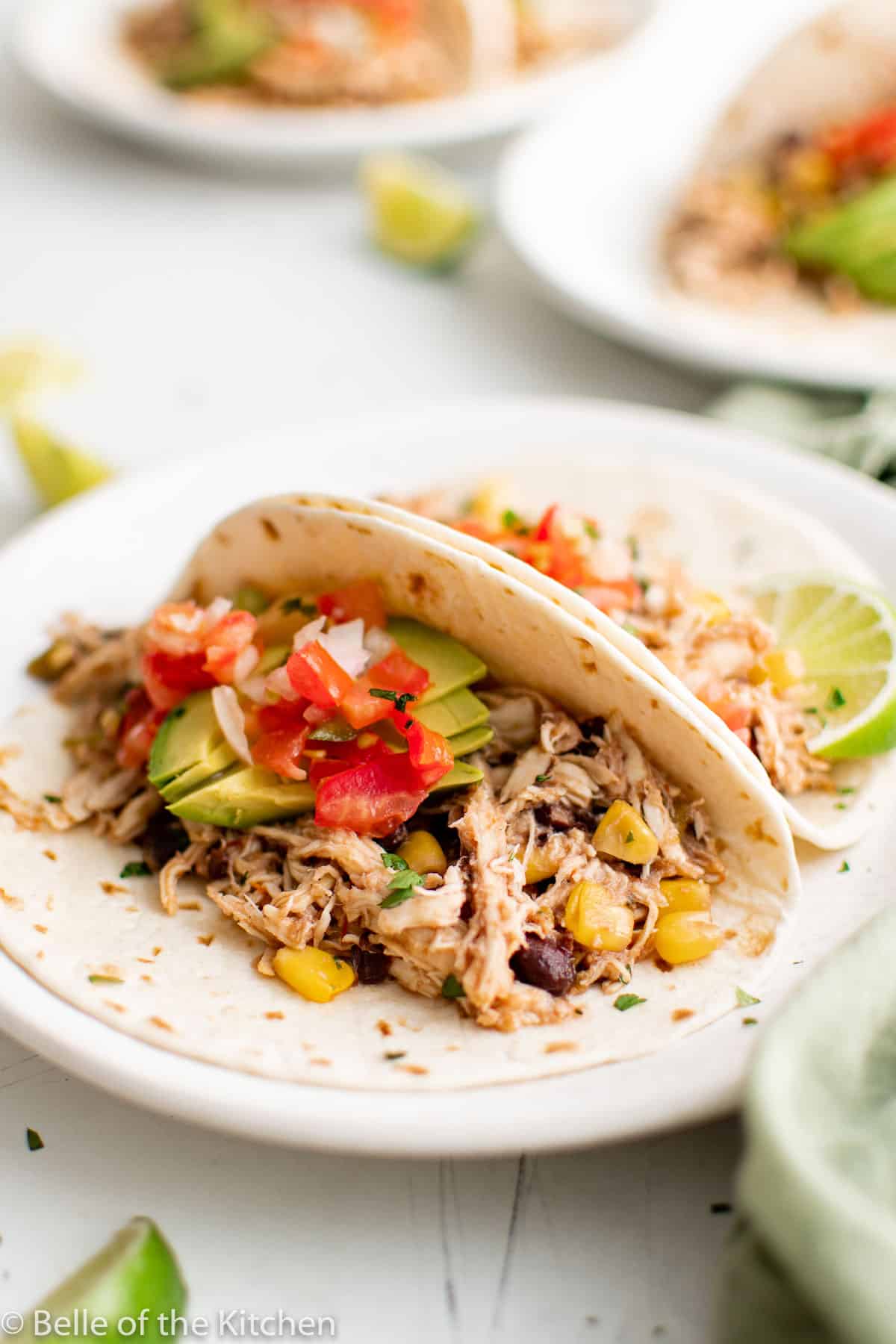 chicken tacos on white plates next to a crockpot.