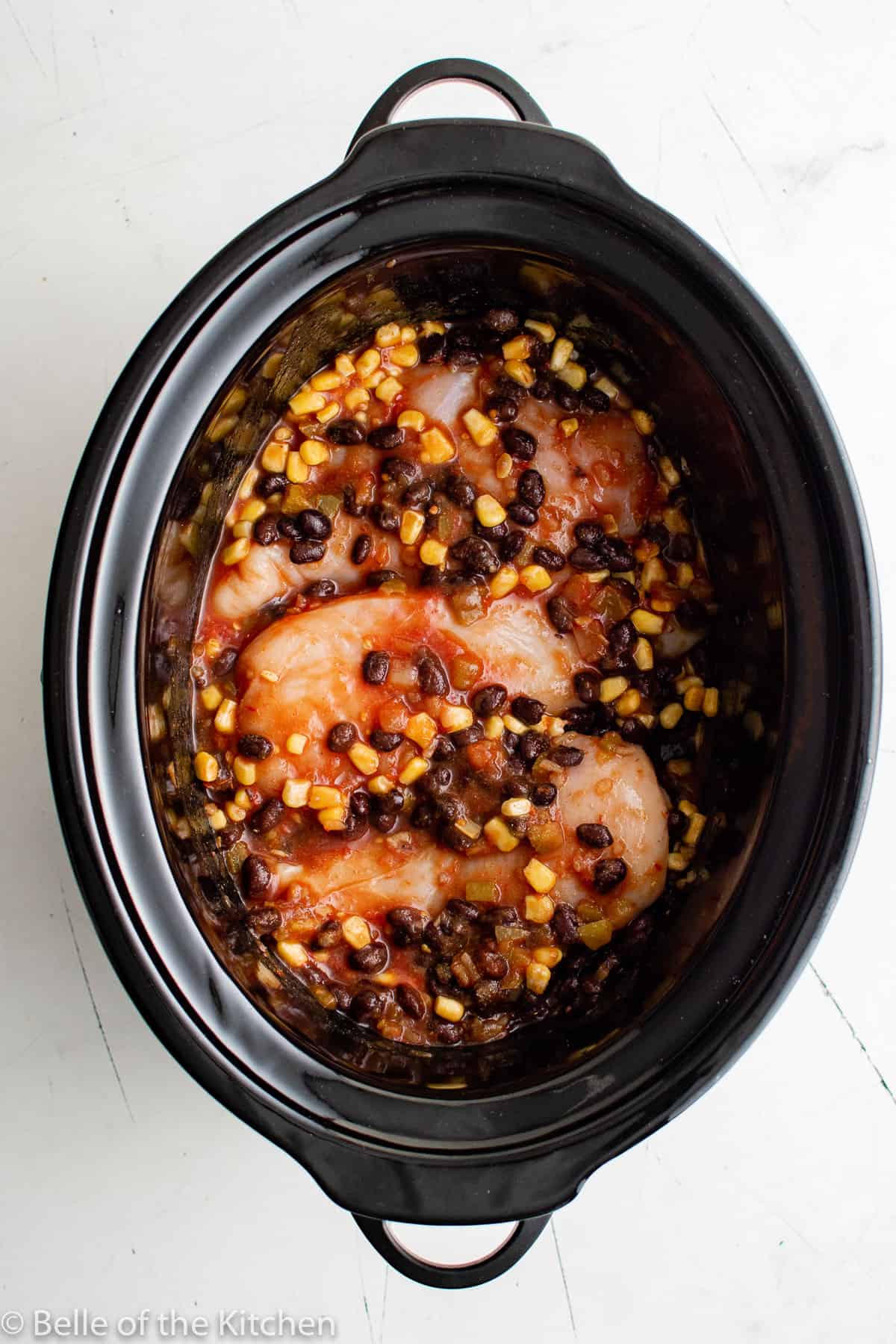 a crockpot full of chicken breasts, corn, salsa, and beans.