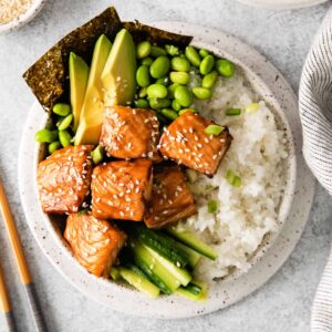 salmon chunks and vegetables on rice in a bowl next to chopsticks