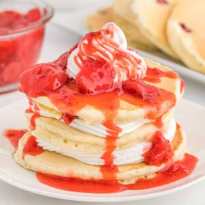 a white plate topped with pancakes, whipped cream, and strawberry sauce