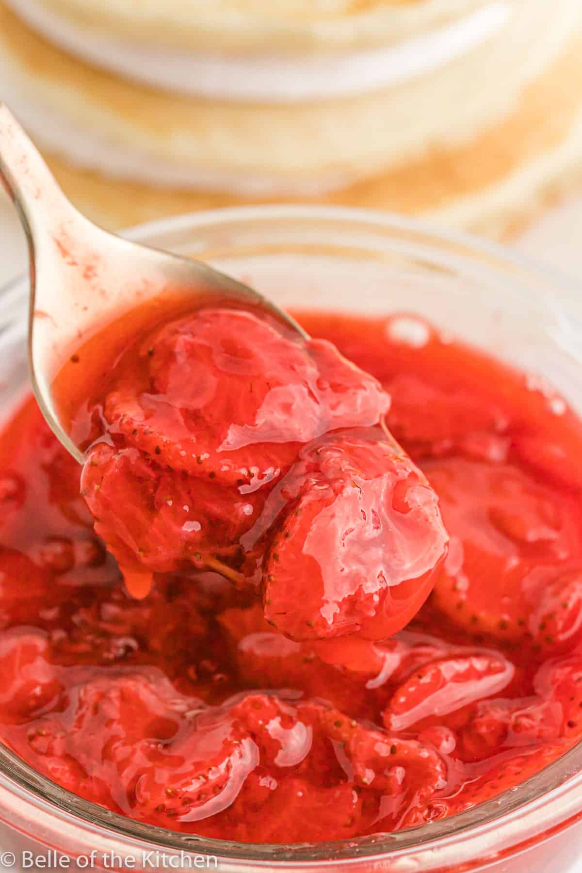 a spoon dipping into a bowl of strawberry sauce