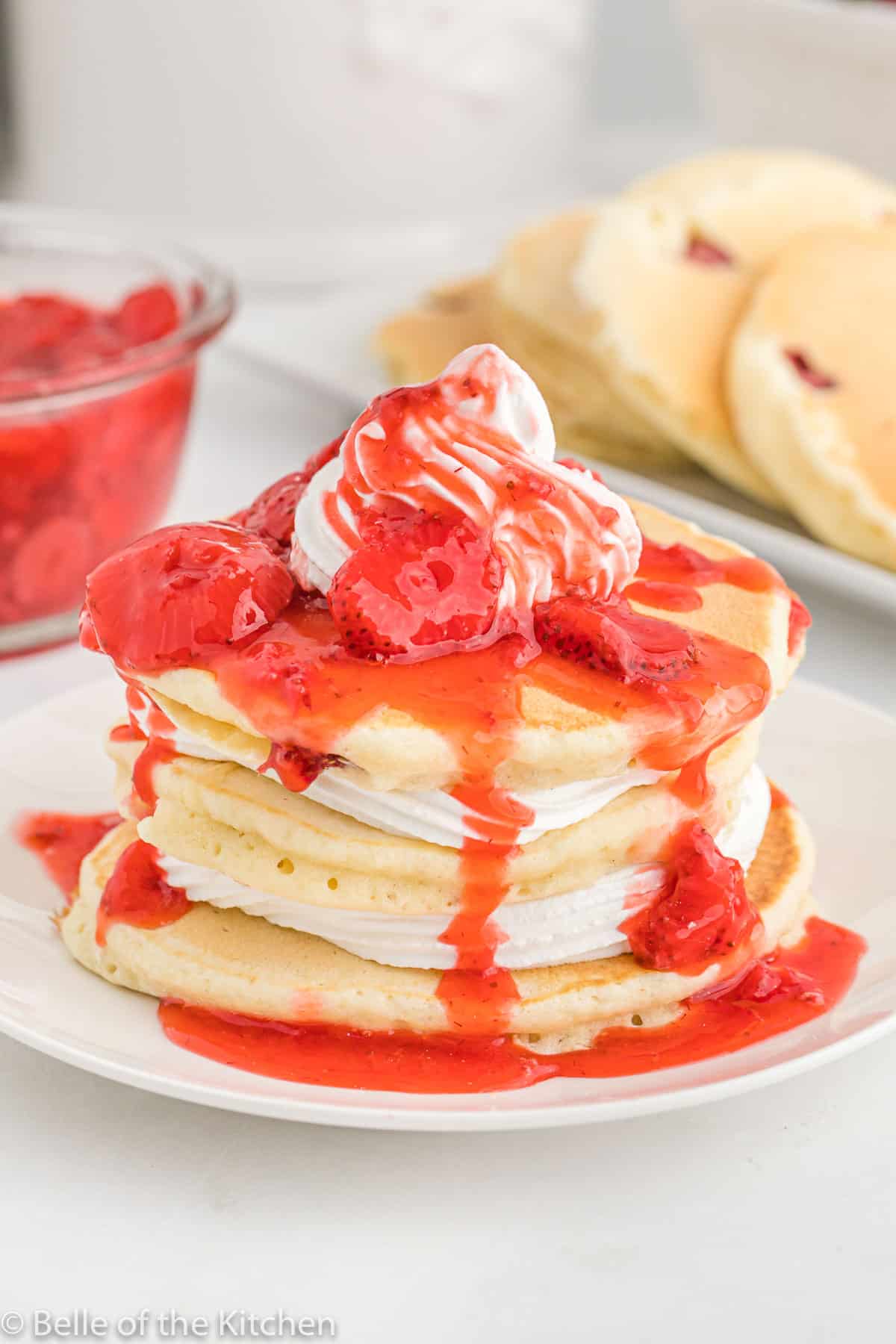 a white plate topped with pancakes, whipped cream, and strawberry sauce