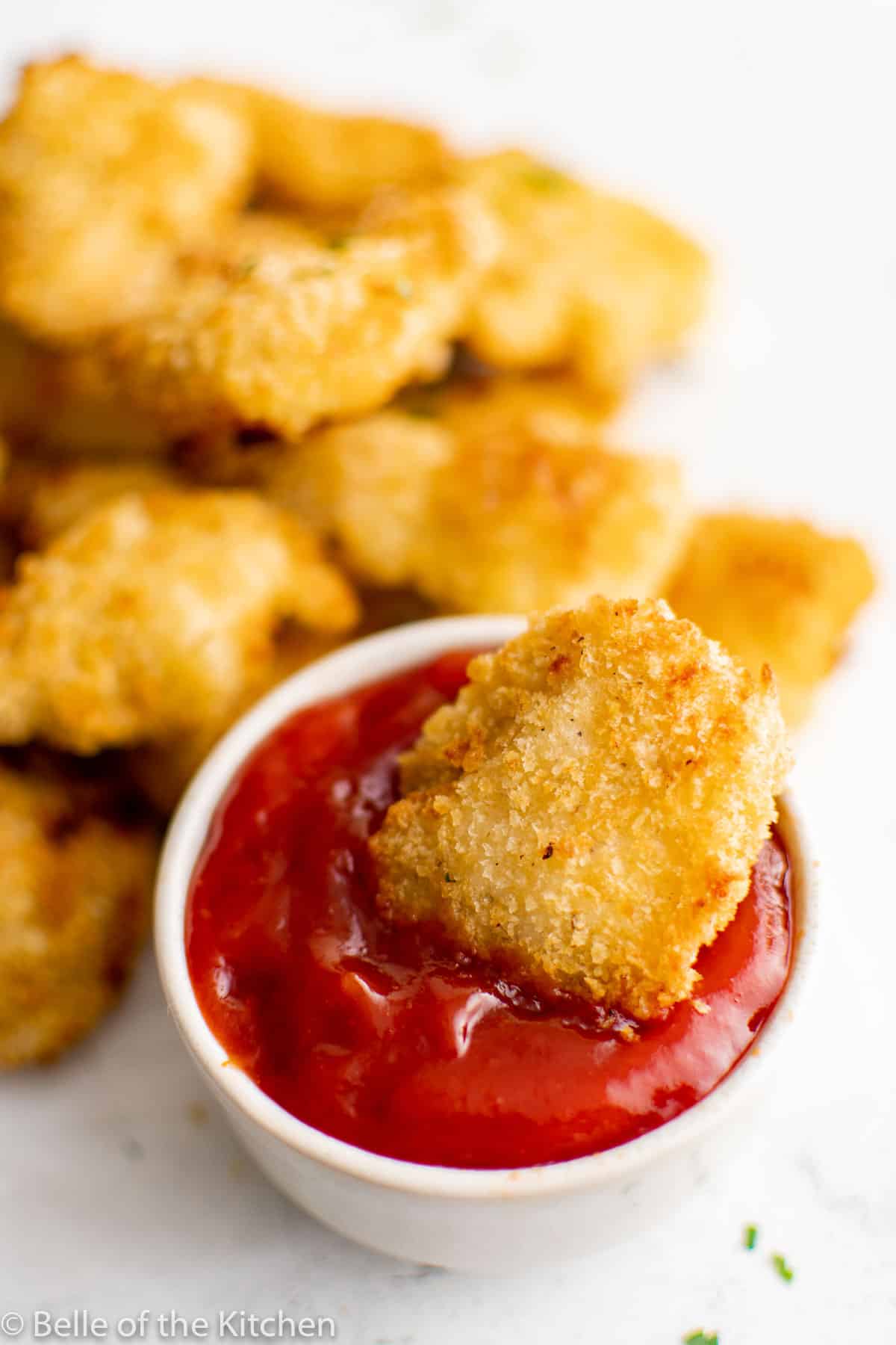 a piece of chicken dunked in a dish of ketchup.